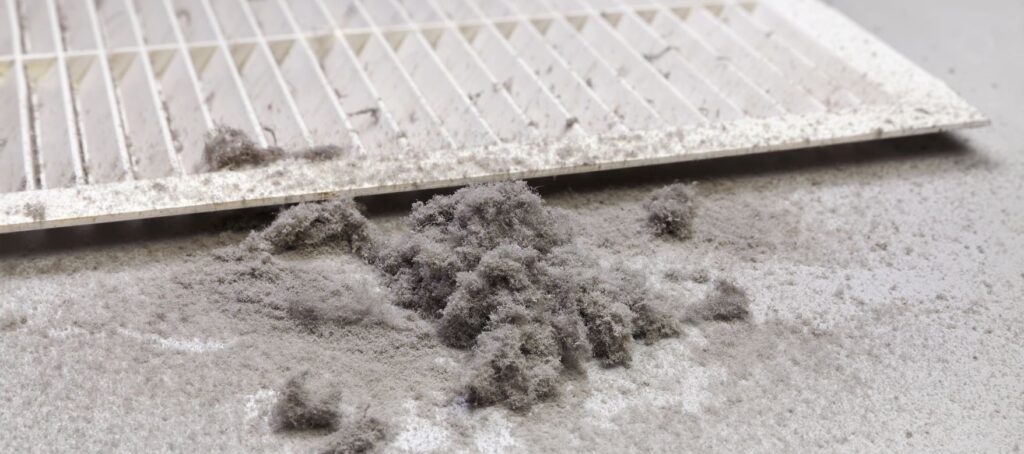 Pile of dust sitting next to an air vent that has been removed from the ducts