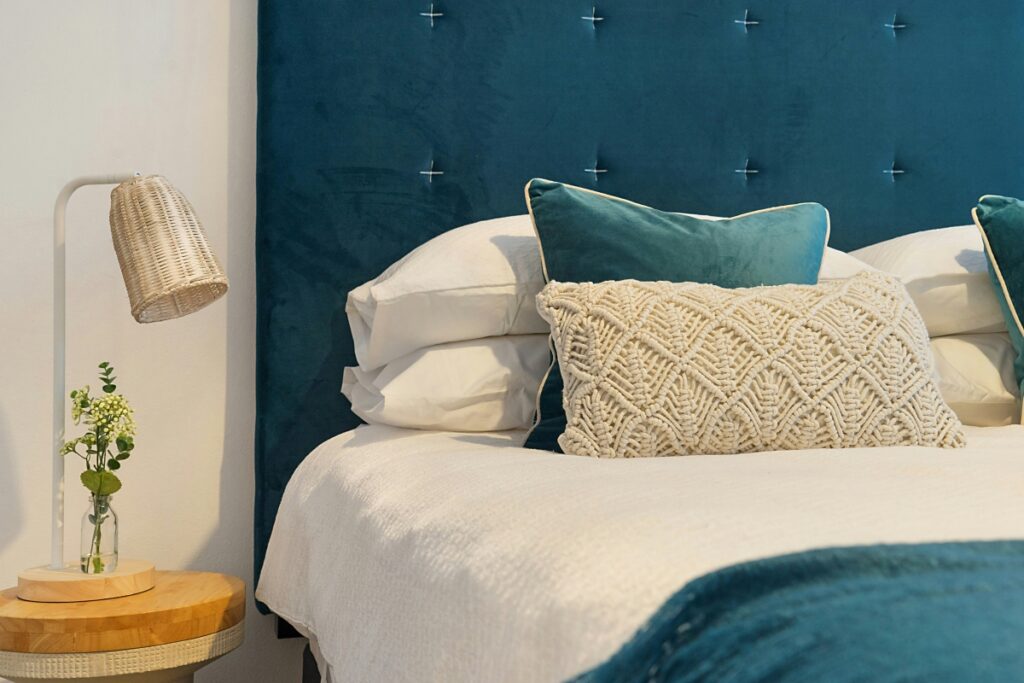 Teal blue and white bed with decorative pillows next to a nightstand