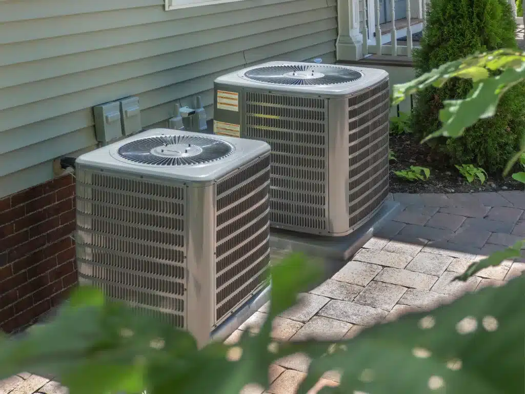 Two outdoor air conditioning units beside a residential home