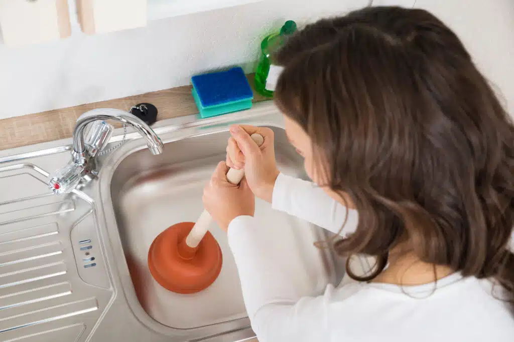 Woman using a plunger to clear a kitchen sink clog