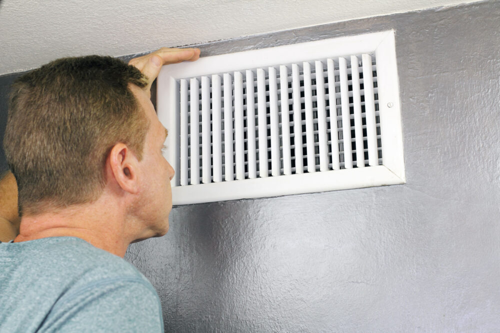 Man examining an outflow air vent grid and duct to see if it needs cleaning. one guy looking into a home air duct to see how clean and healthy it is.